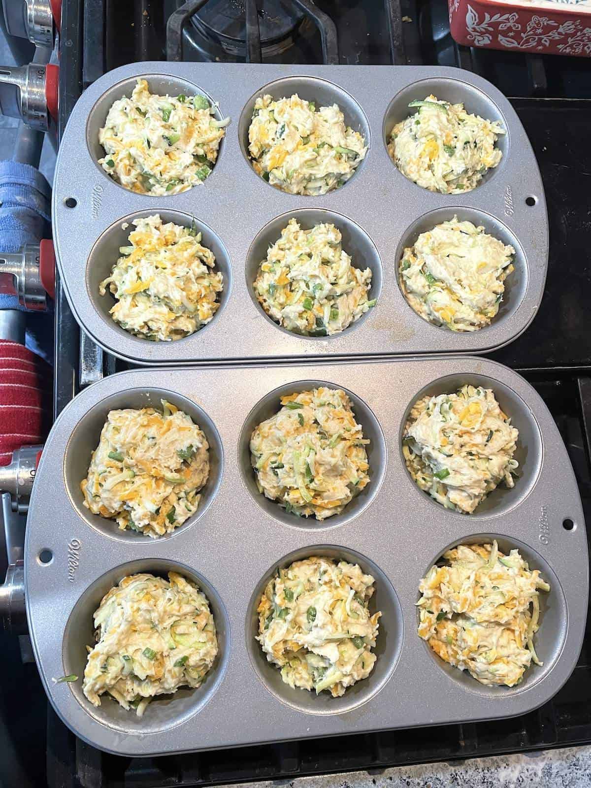 Jumbo zucchini muffin batter with cheddar and jalapeños in a muffin tin.