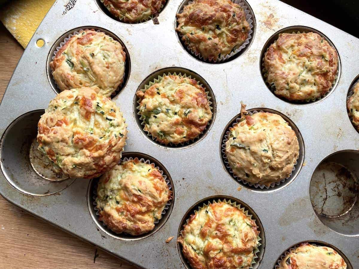 A muffin tin with baked savory zucchini muffins with cheese in them.