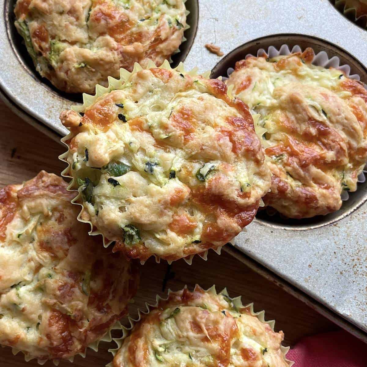 Savory zucchini muffins with cheese on top of a muffin tin.