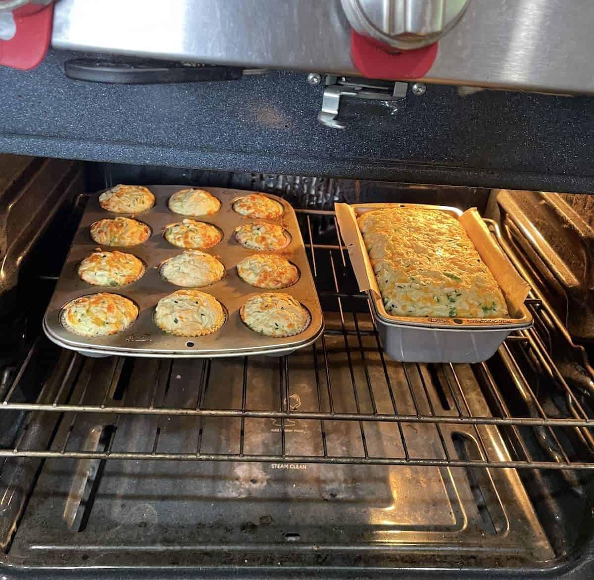 A pan of savory zucchini muffins and a loaf of zucchini bread baking in the oven.