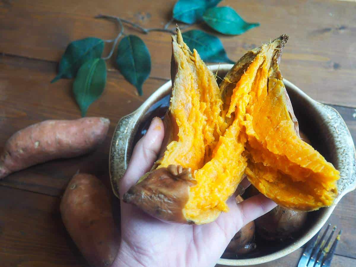 A hand holding a cooked sweet potato over a brown bowl.