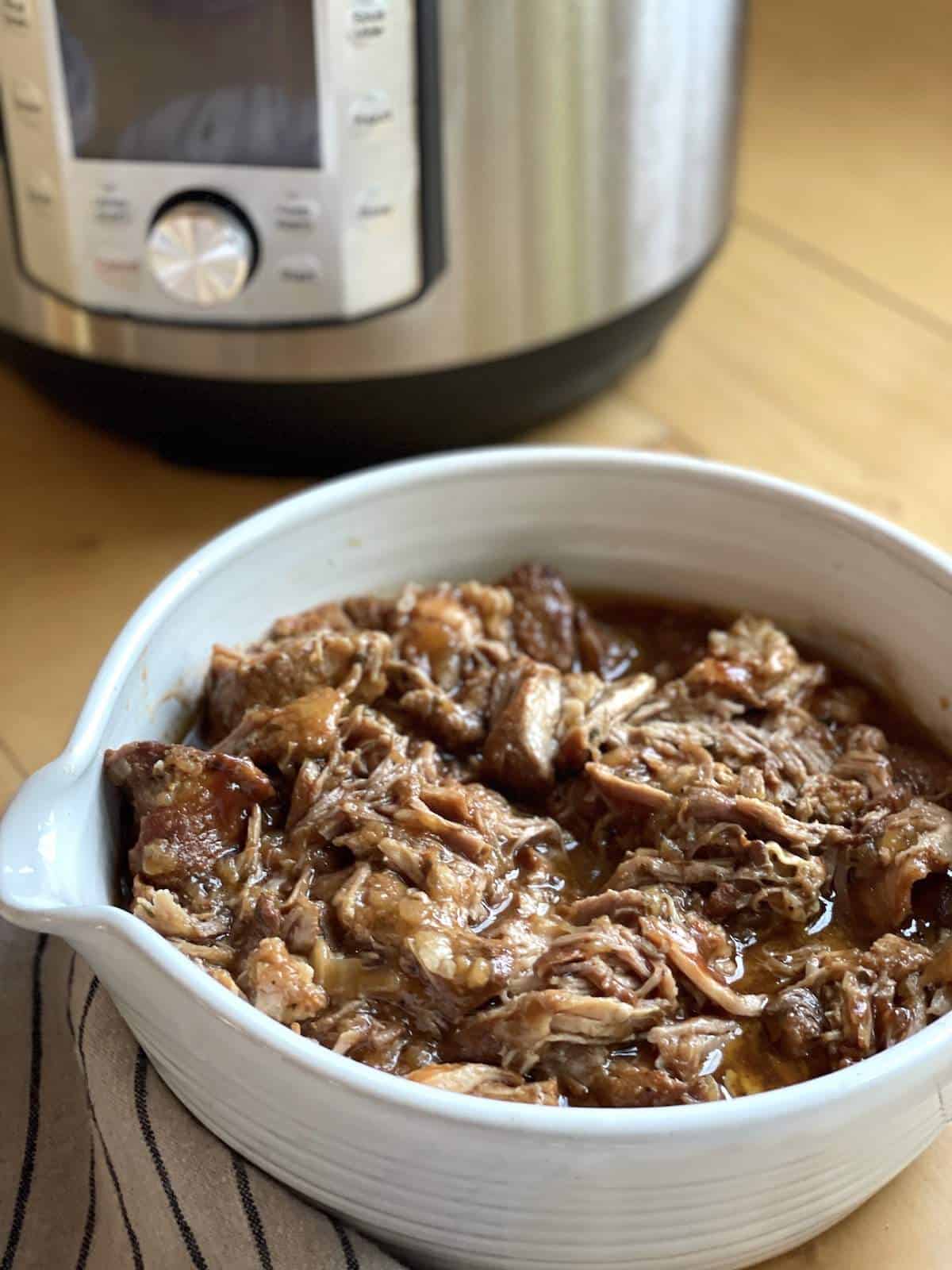 A white bowl of Instant Pot country style ribs in front of an Instant Pot.