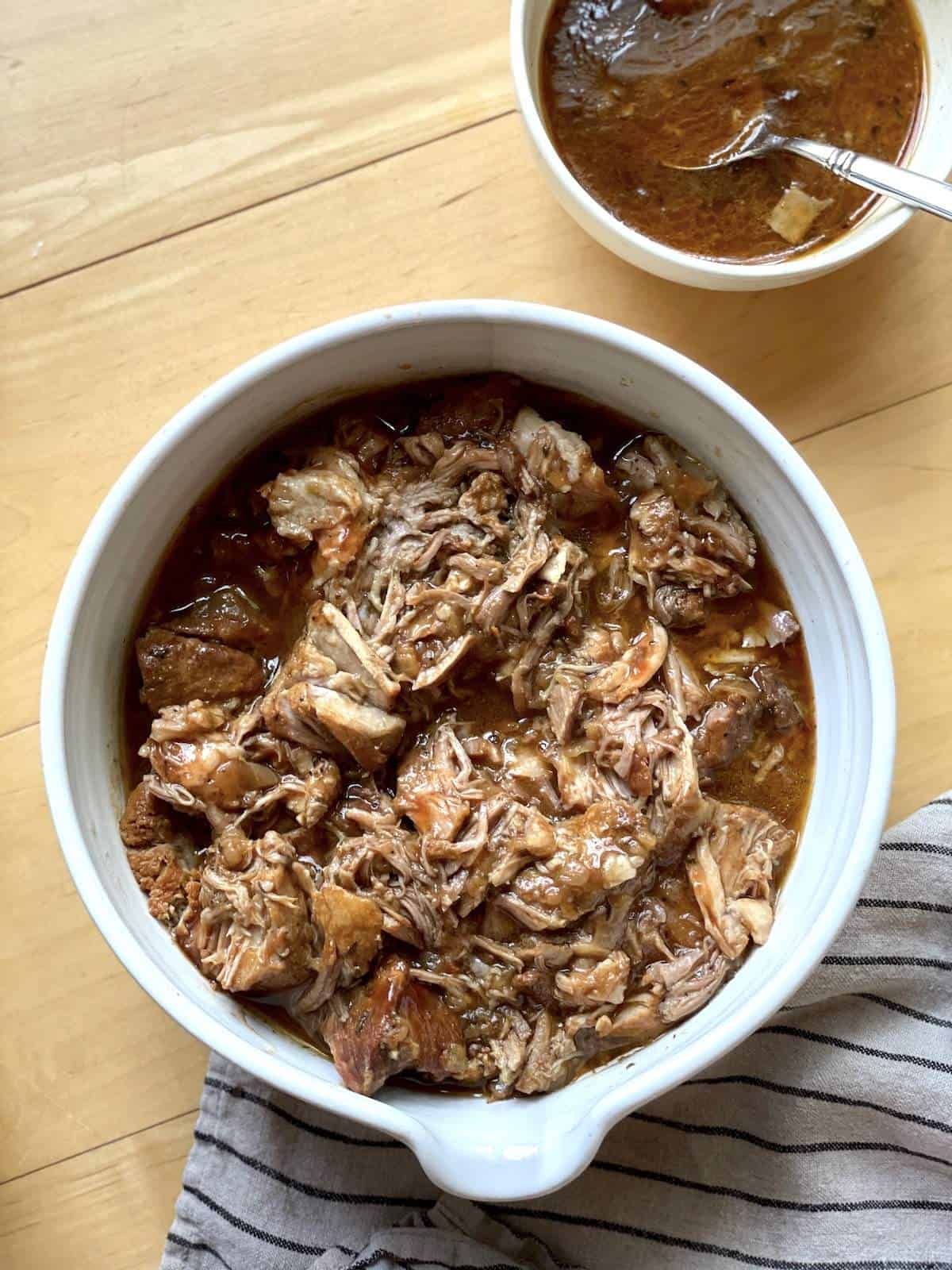 A white bowl of instant pot country style ribs with a bowl of sauce.