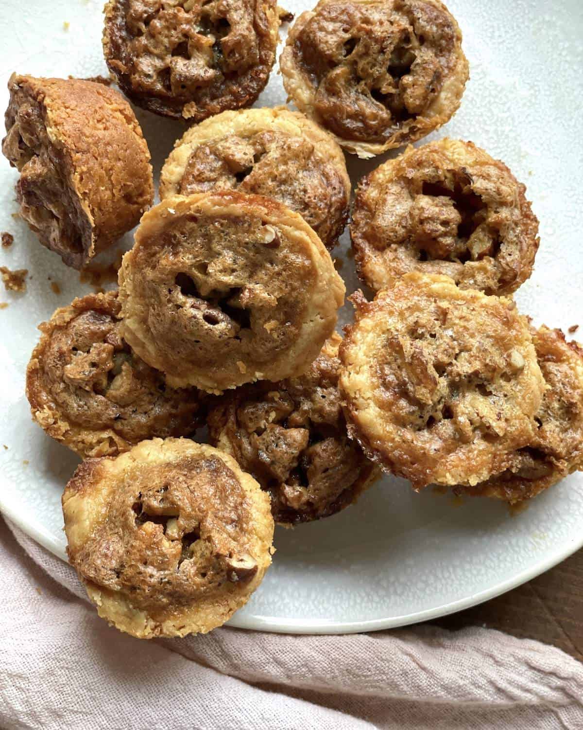 A pile of pecan pie tartlets on a white plate.