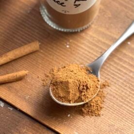 Homemade apple pie spice on a spoon in front of a jar of the spice blend.
