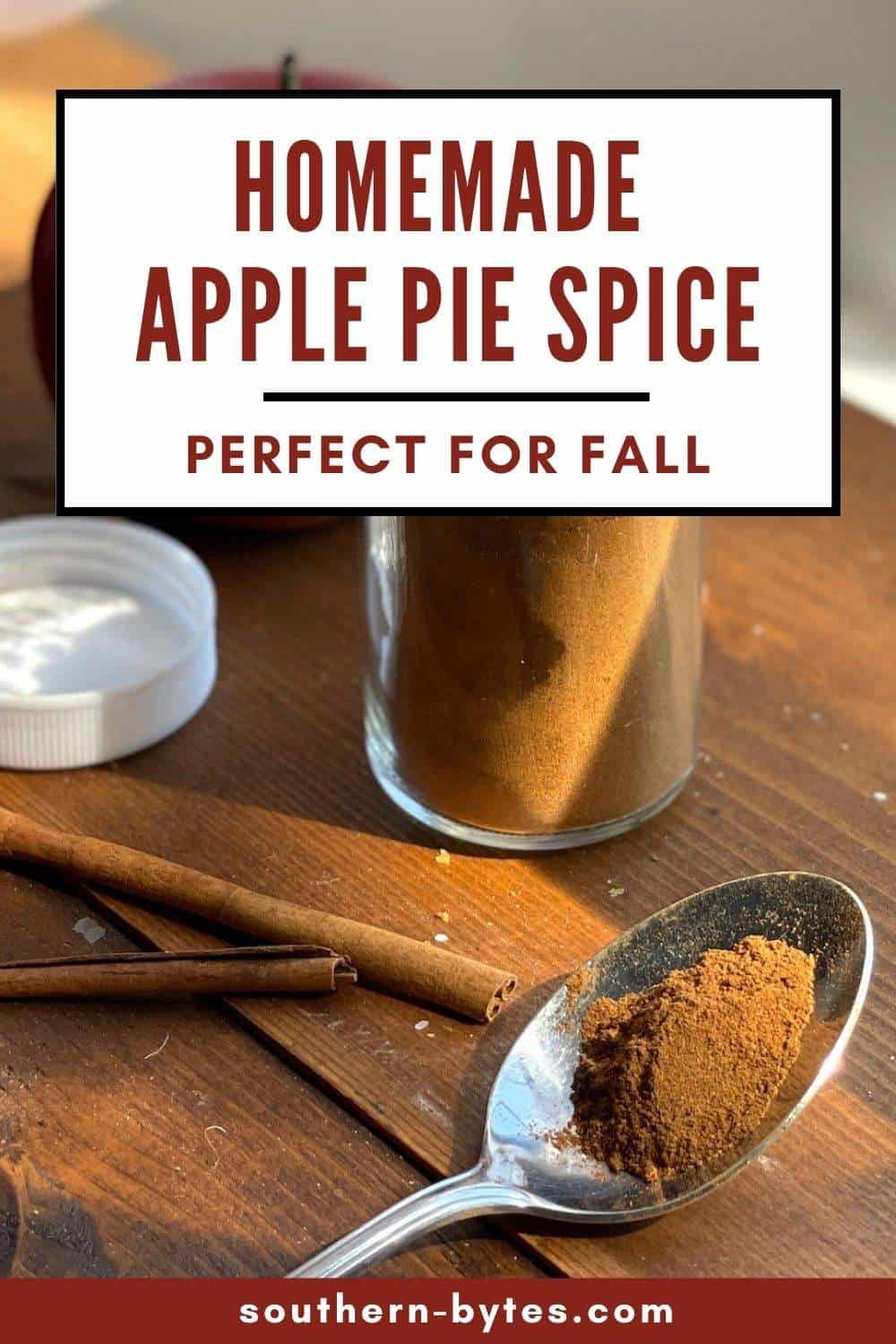 A pin image of an open jar of apple pie spice mix with some on a spoon and cinnamon sticks.