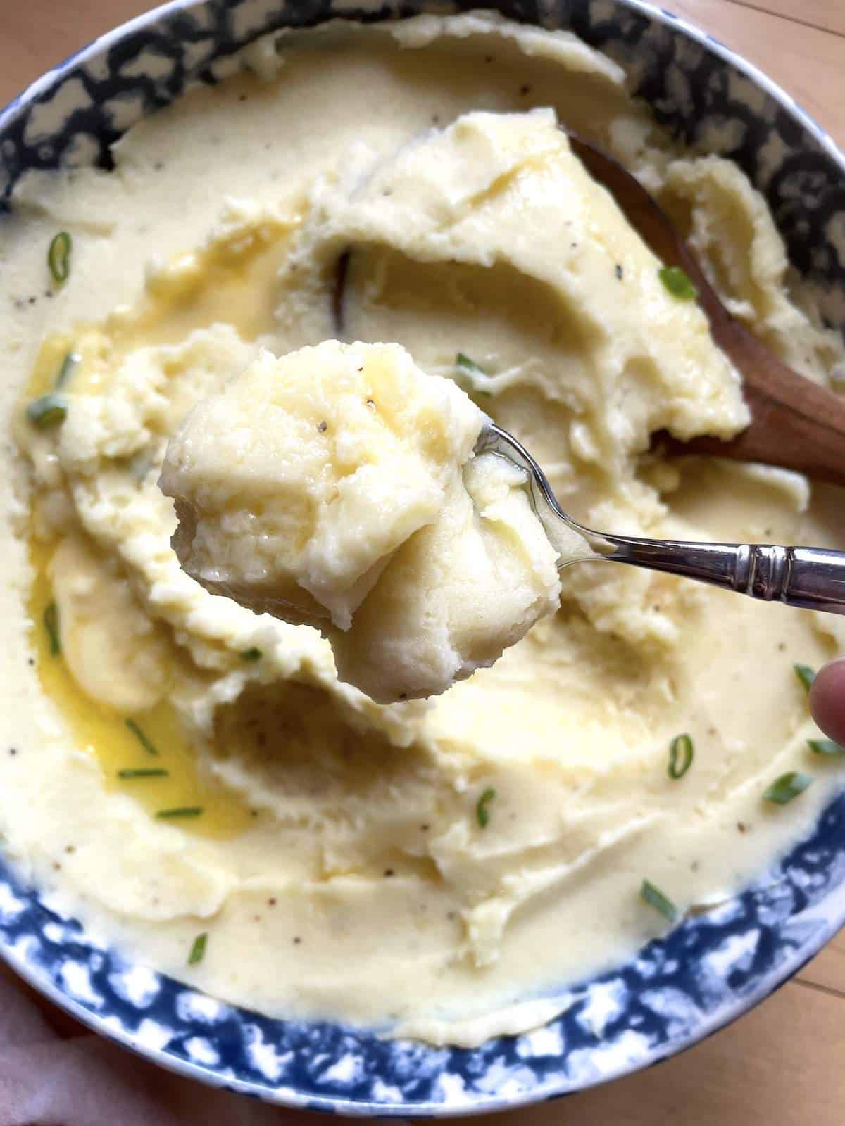 A spoonful of buttermilk mashed potatoes over a bowl of mashed potatoes.