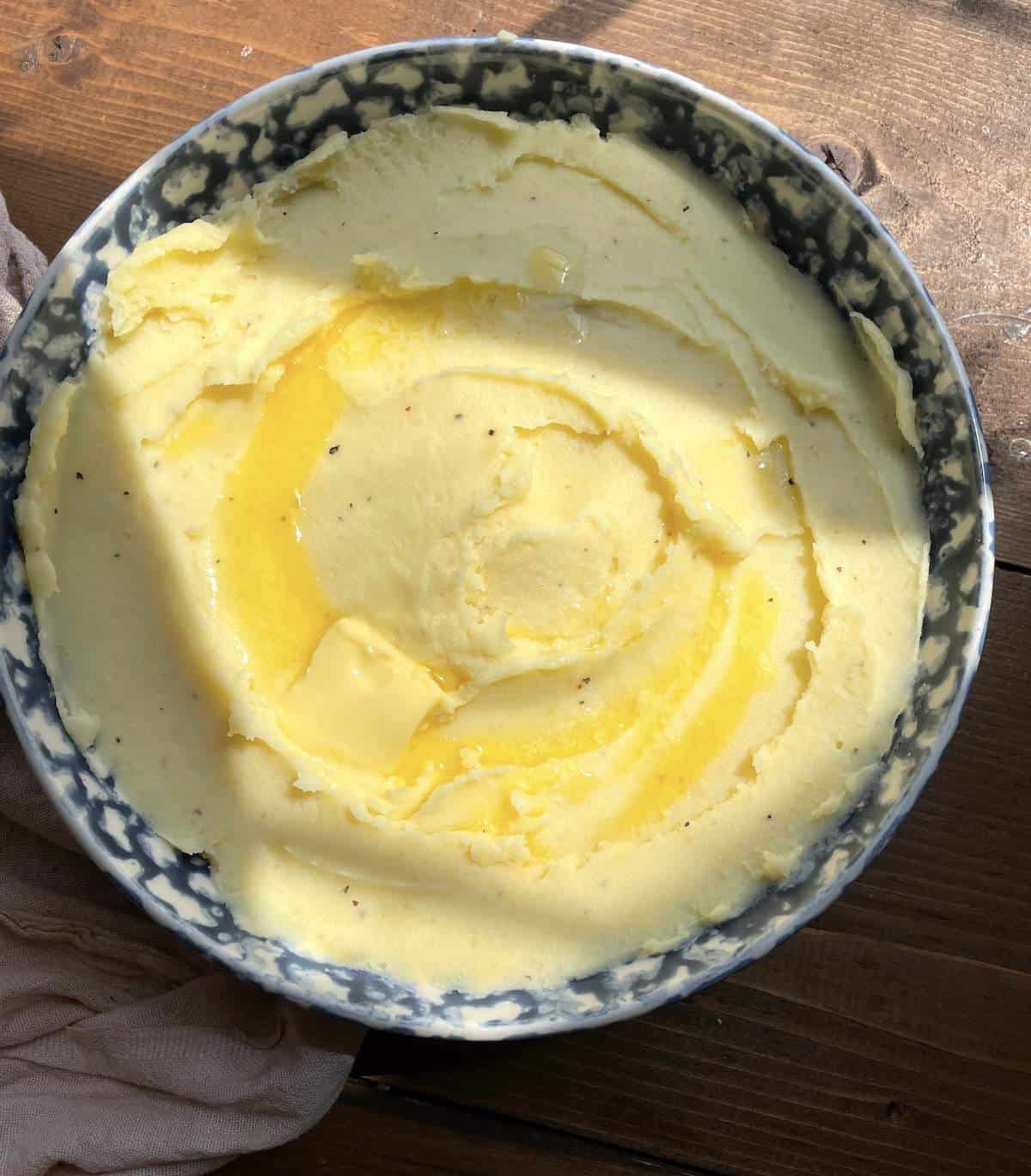 A bowl of buttermilk mashed potatoes in the afternoon sunlight with melted butter on top.
