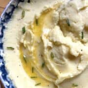 A bowl of buttermilk mashed potatoes with a pool of melted butter and fresh chives on top, zoomed in.