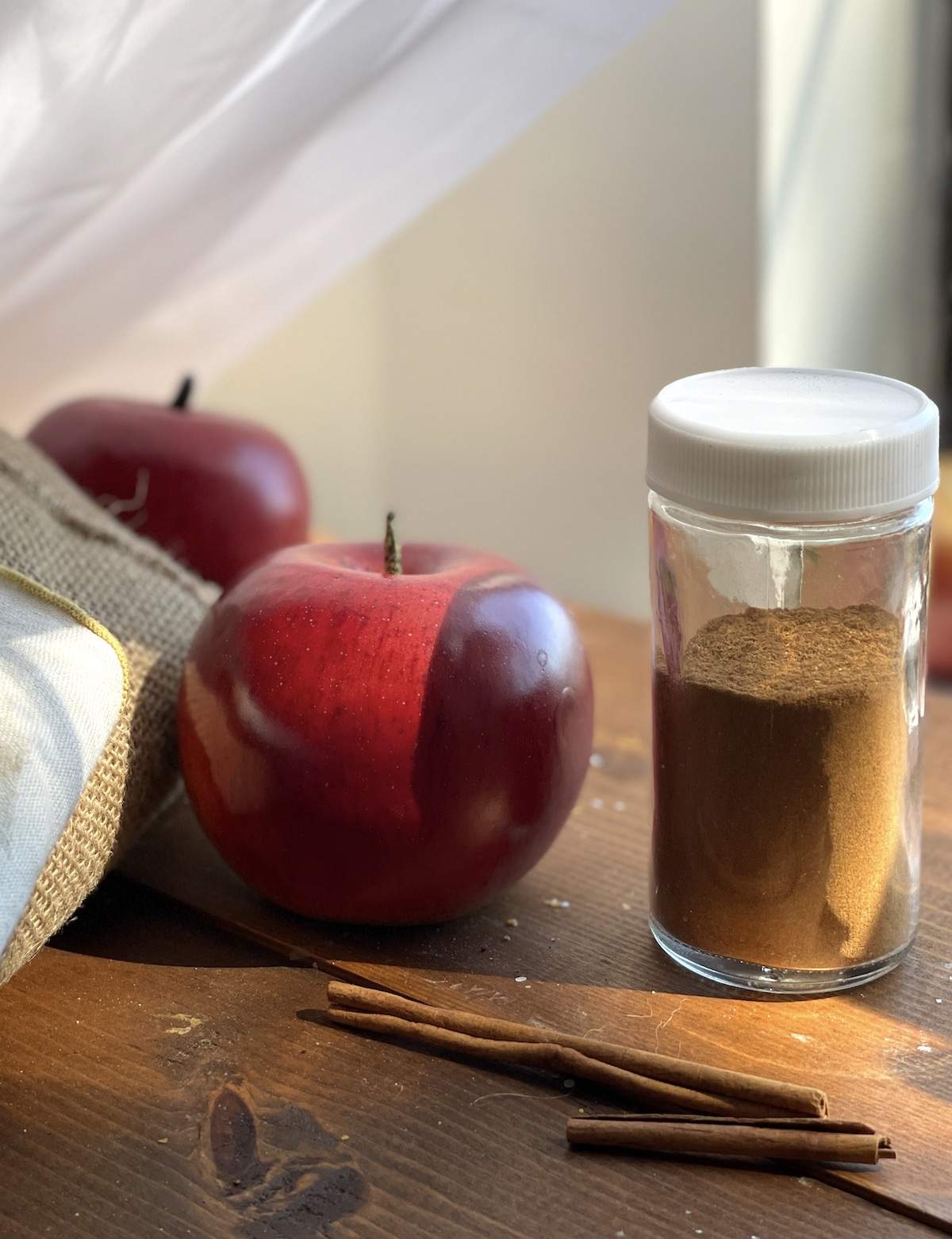 A jar of homemade apple pie spice next to an apple.