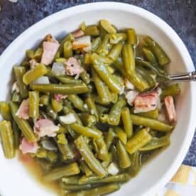 A white bowl of southern green beans and bacon on a gray background.