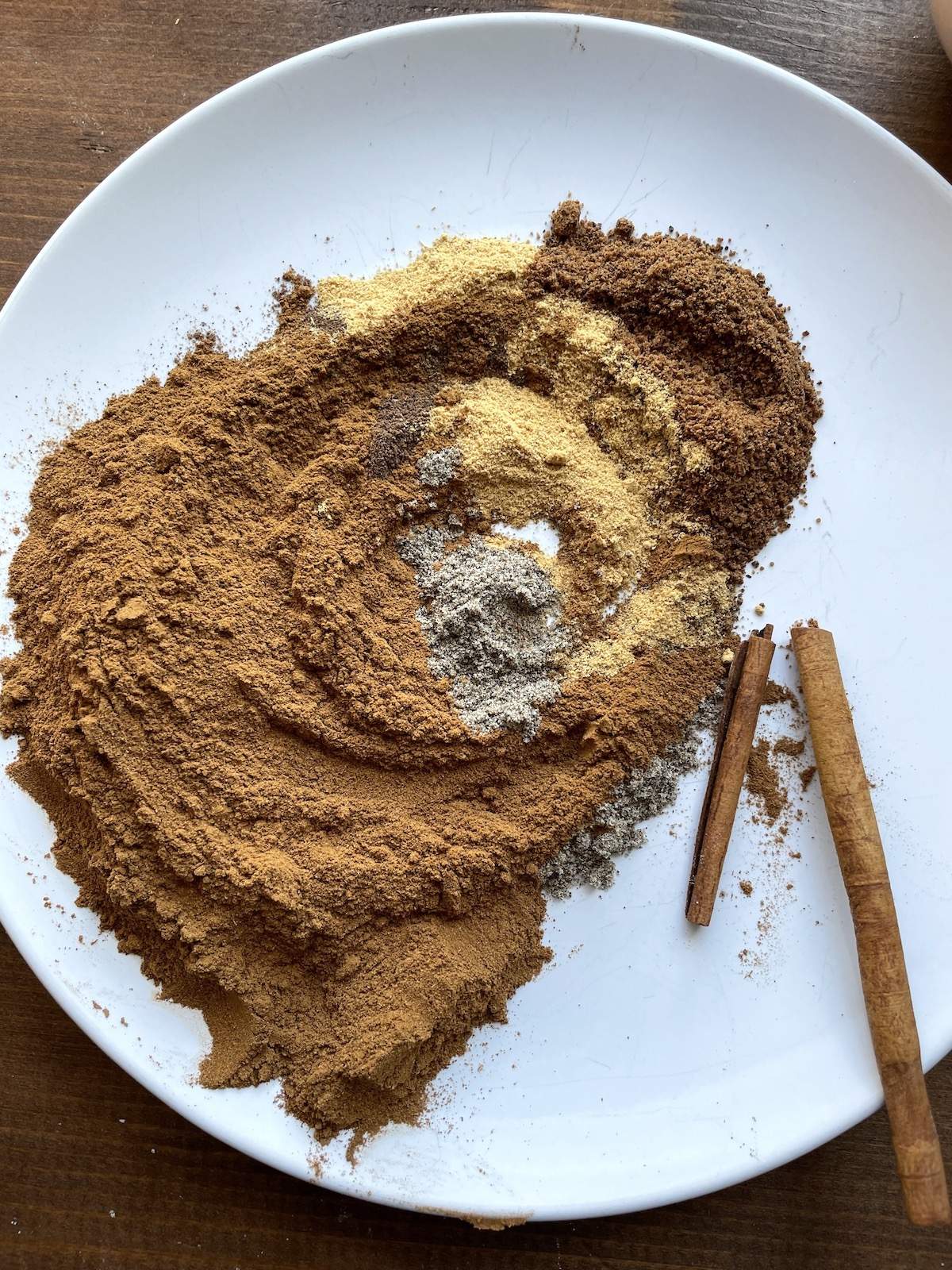 The ingredients in apple pie spice mix on a plate swirled together on a white plate.