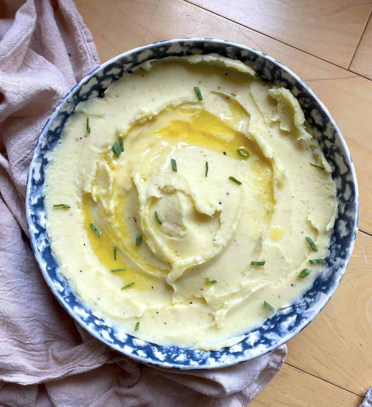 A bowl of buttermilk mashed potatoes topped with melted butter and diced fresh chives.