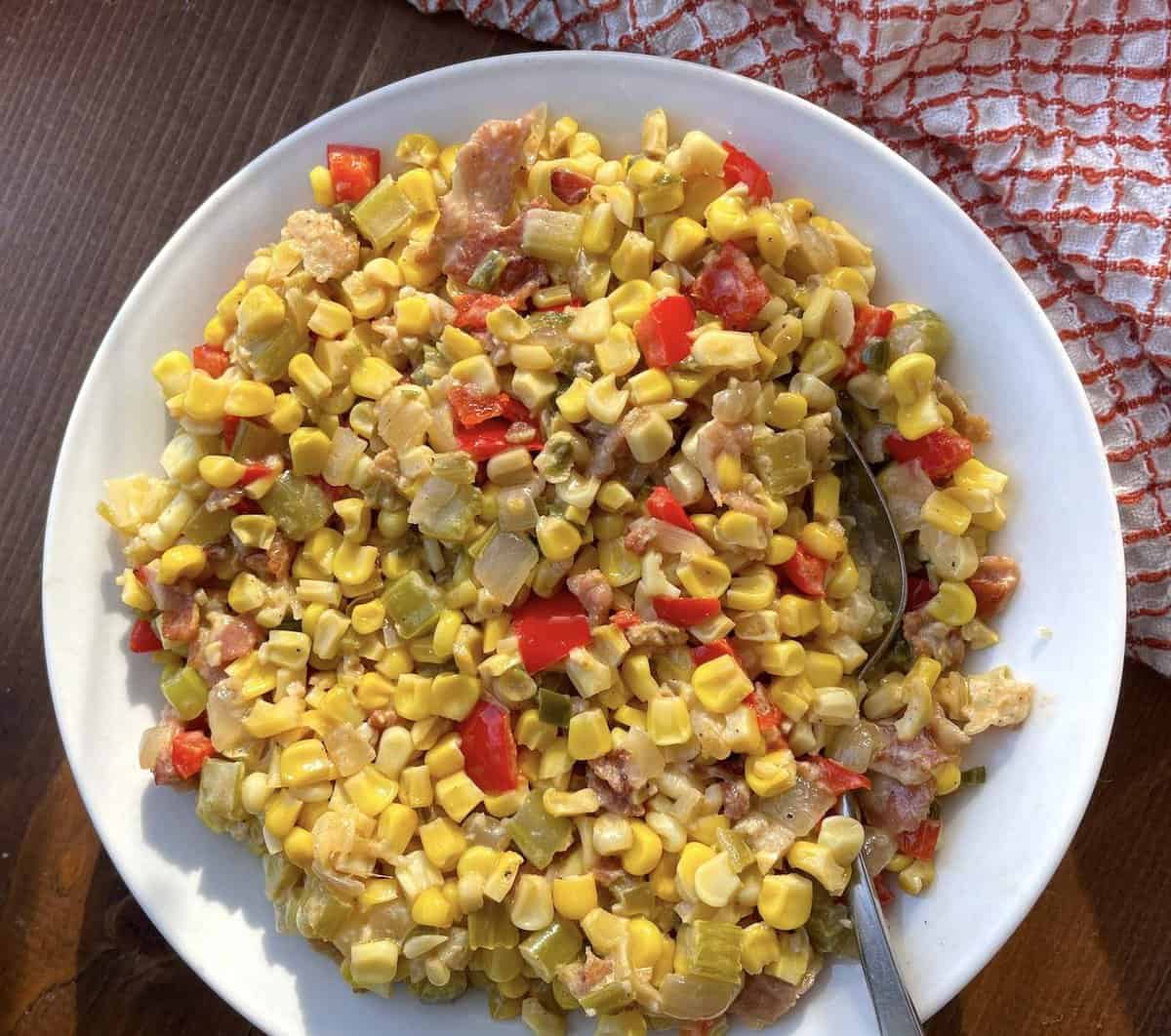 A bowl of corn maque choux with a silver spoon.
