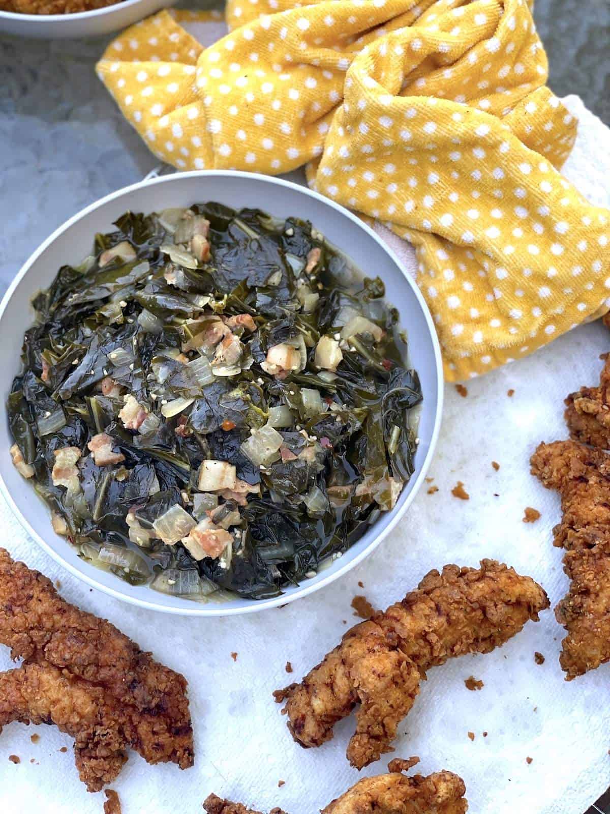 A bowl of collard greens on a paper towel where fried chicken is draining.