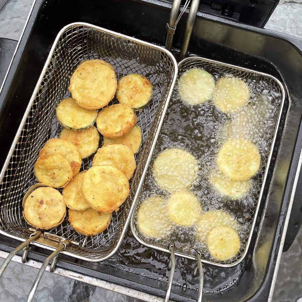 A deep fryer with two baskets of yellow squash and zucchini frying in it.