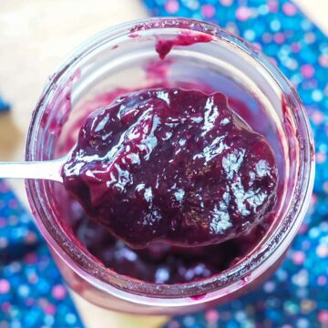 A jar of instant pot blueberry jam being scooped out with a spoon.