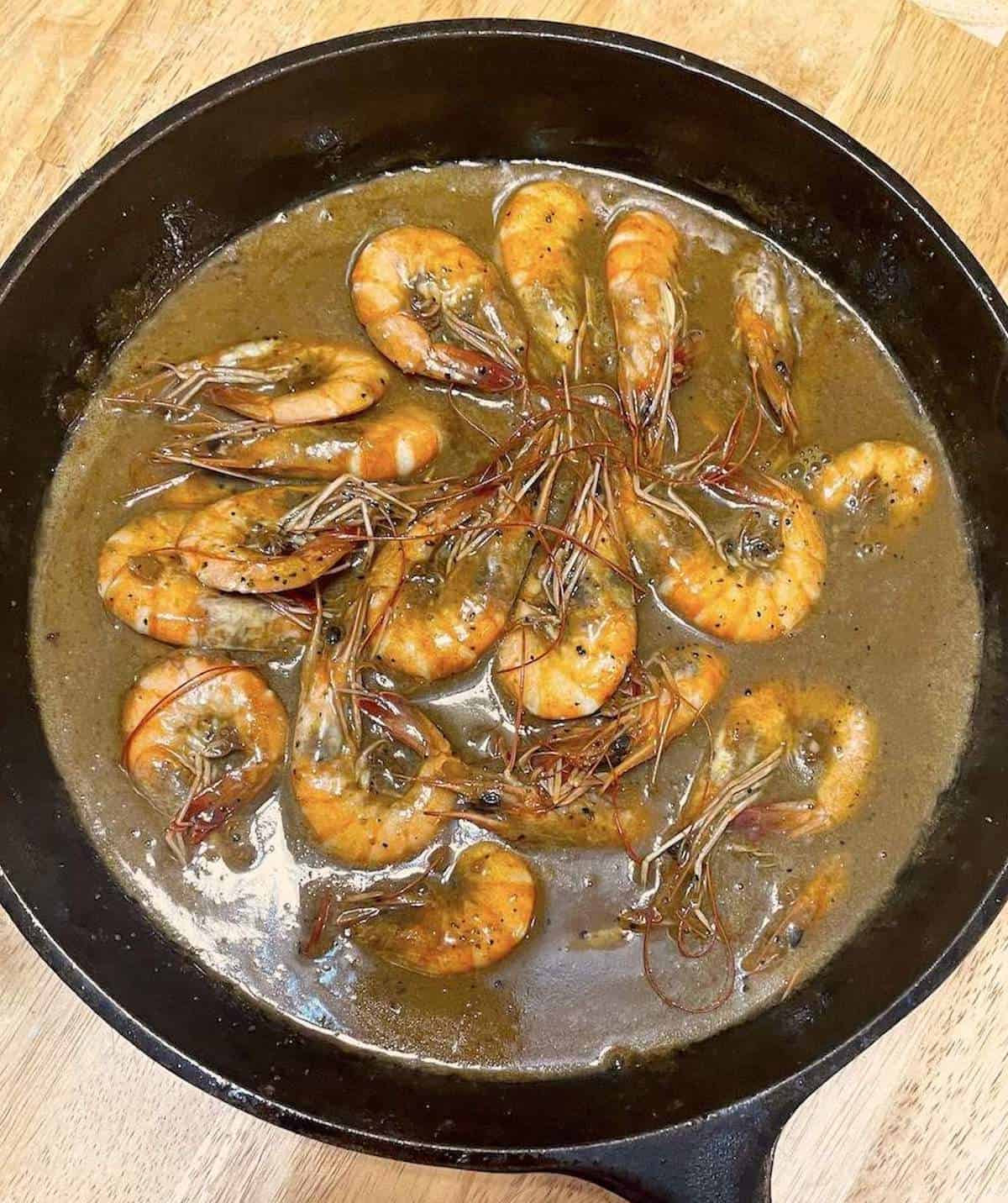 Cooked BBQ shrimp smothered in sauce in a cast iron skillet.