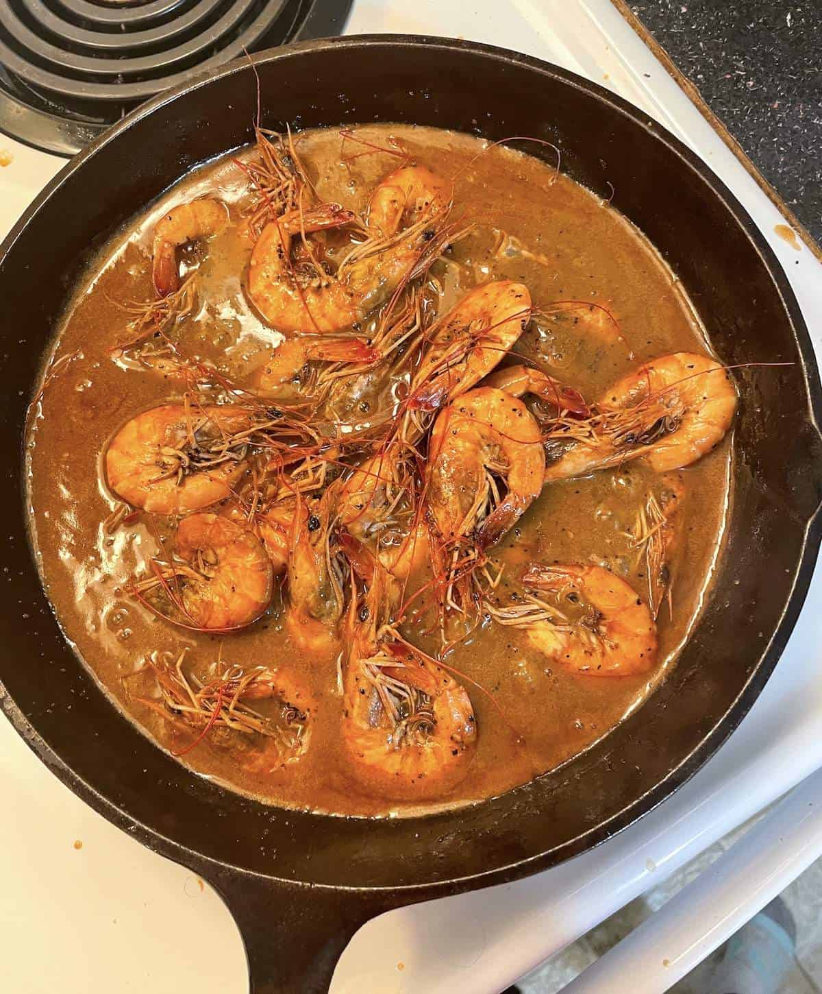 A cast iron pan with New Orleans BBQ shrimp cooking in a skillet.