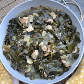 A bowl of southern collard greens on a metal rack with a yellow towel.