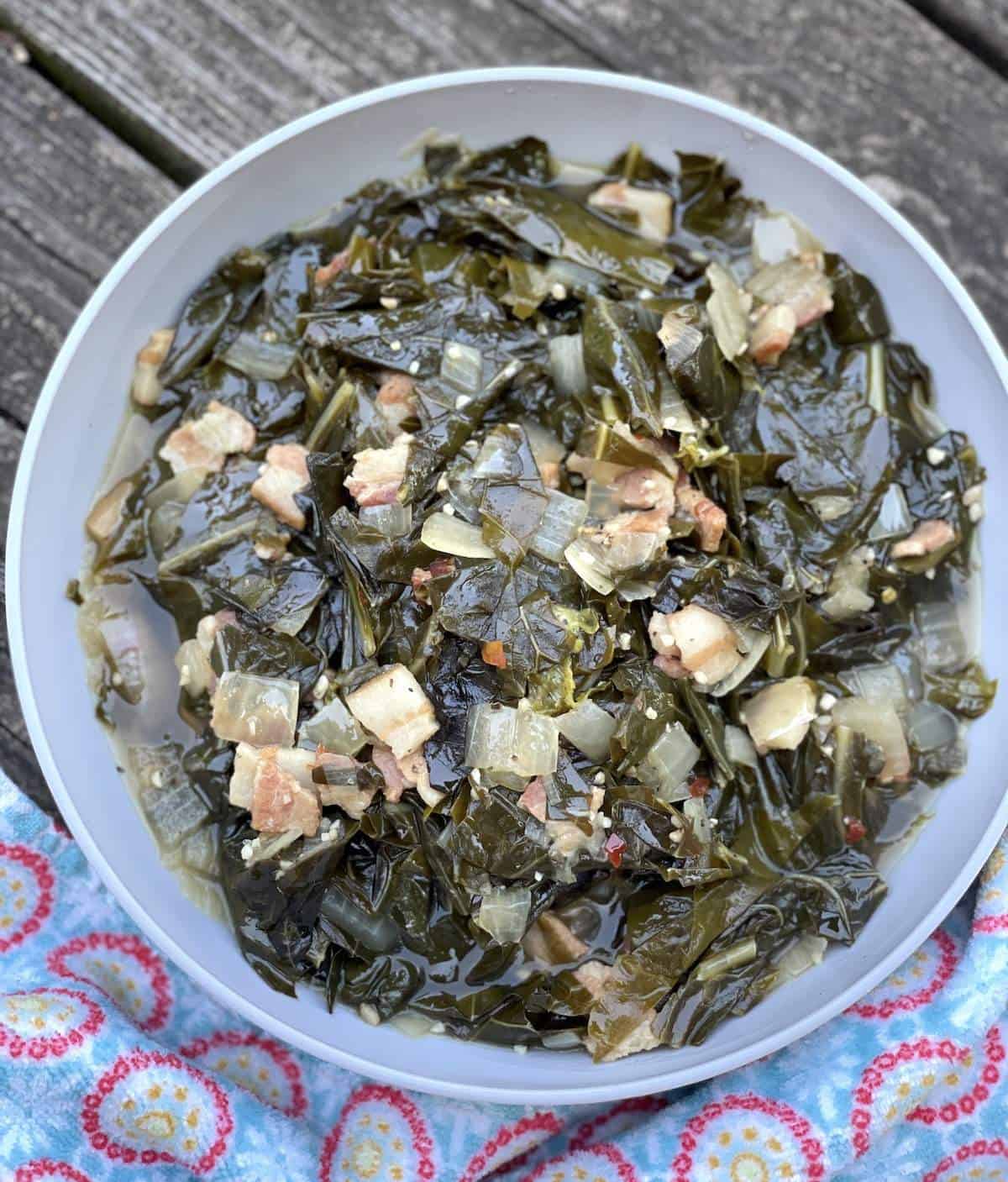 A bowl of collard greens with smoked turkey on a wood background with a floral towel.