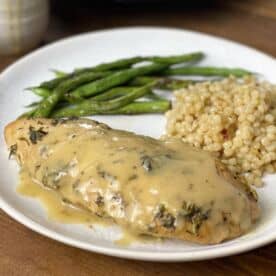 A cooked turkey tenderloin with Israeli couscous and green beans on a white plate.
