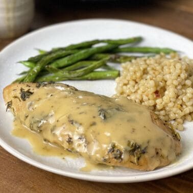 A cooked turkey tenderloin with Israeli couscous and green beans on a white plate.