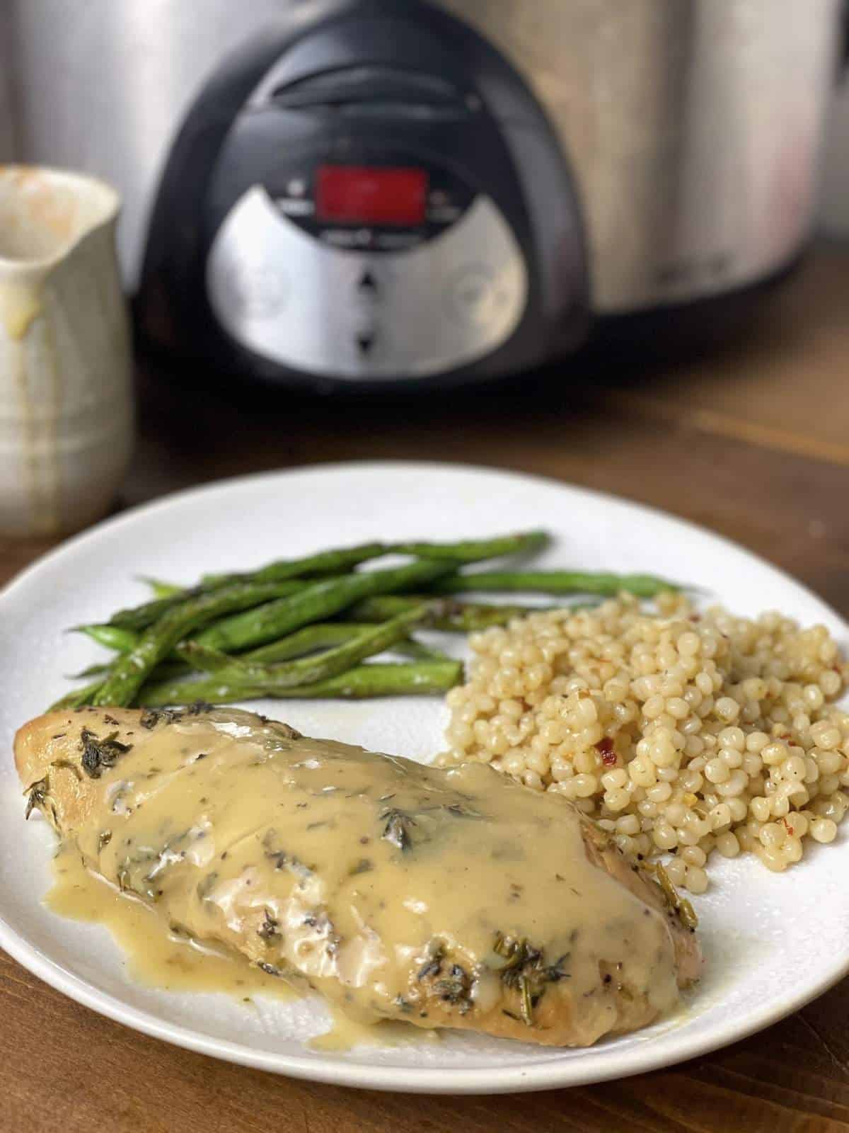 A cooked turkey tenderloin with Israeli couscous and green beans on a plate in front of a crockpot.