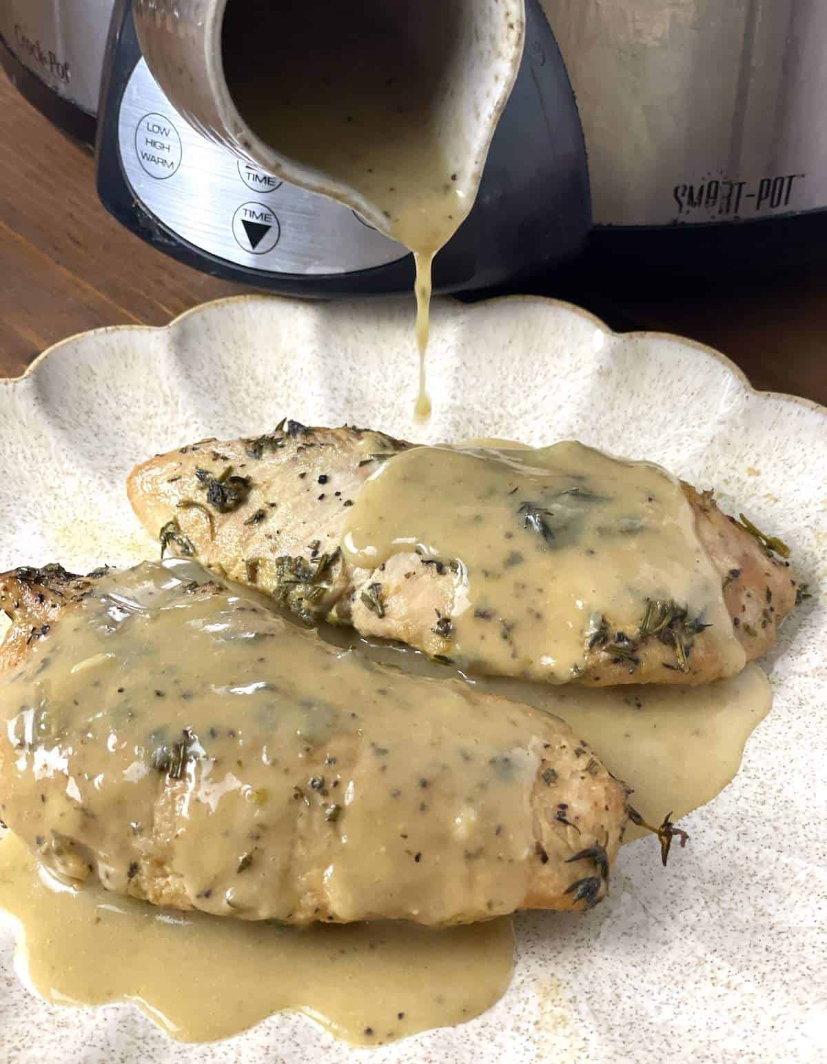 Two whole turkey tenderloins on a scalloped plate with gravy being poured over the top.