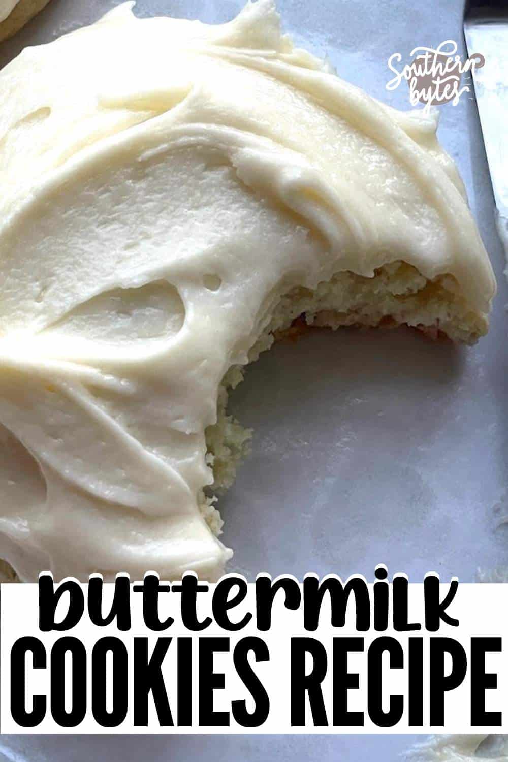 A pin image of a buttermilk cookie with thick frosting and a bite taken out of it.