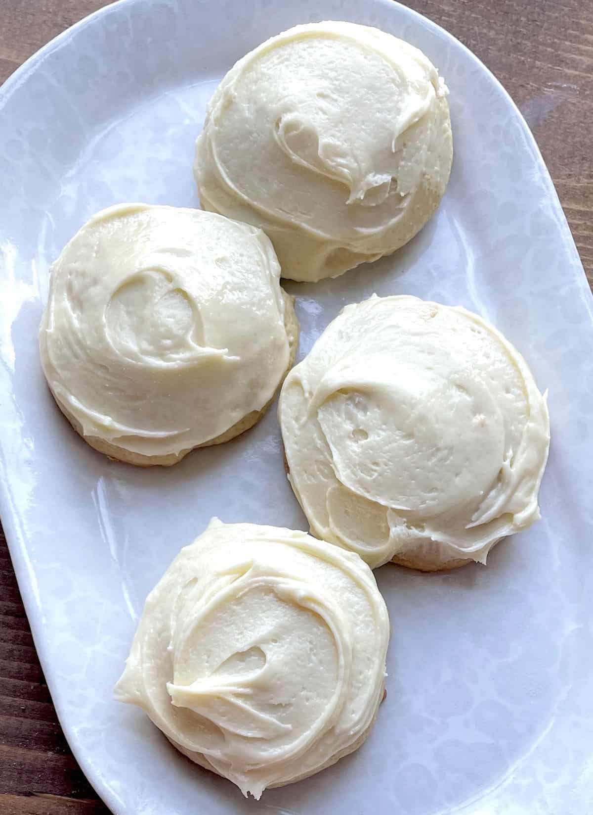 Four frosted buttermilk cookies on a white plate.