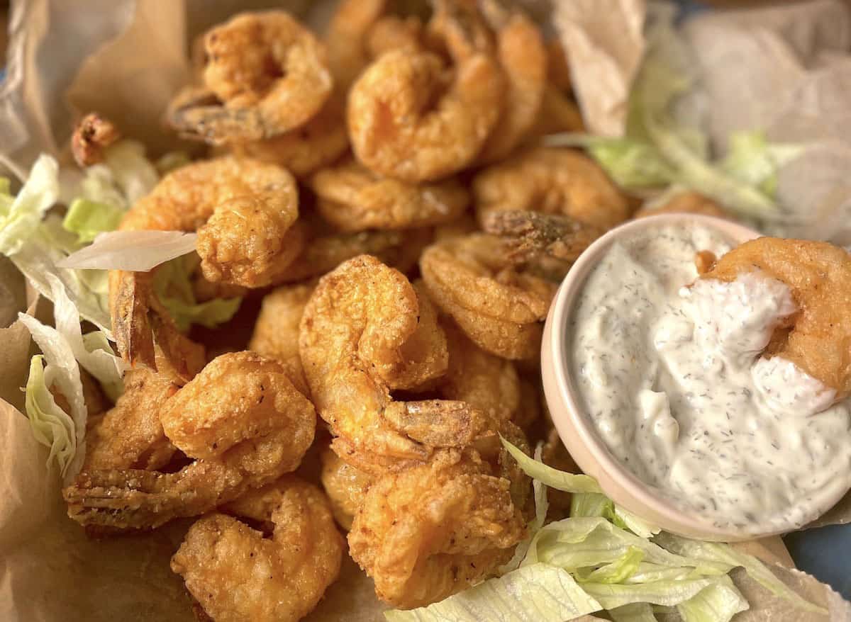 An up close image of crispy fried shrimp with the tails on and a small bowl of tartar sauce.
