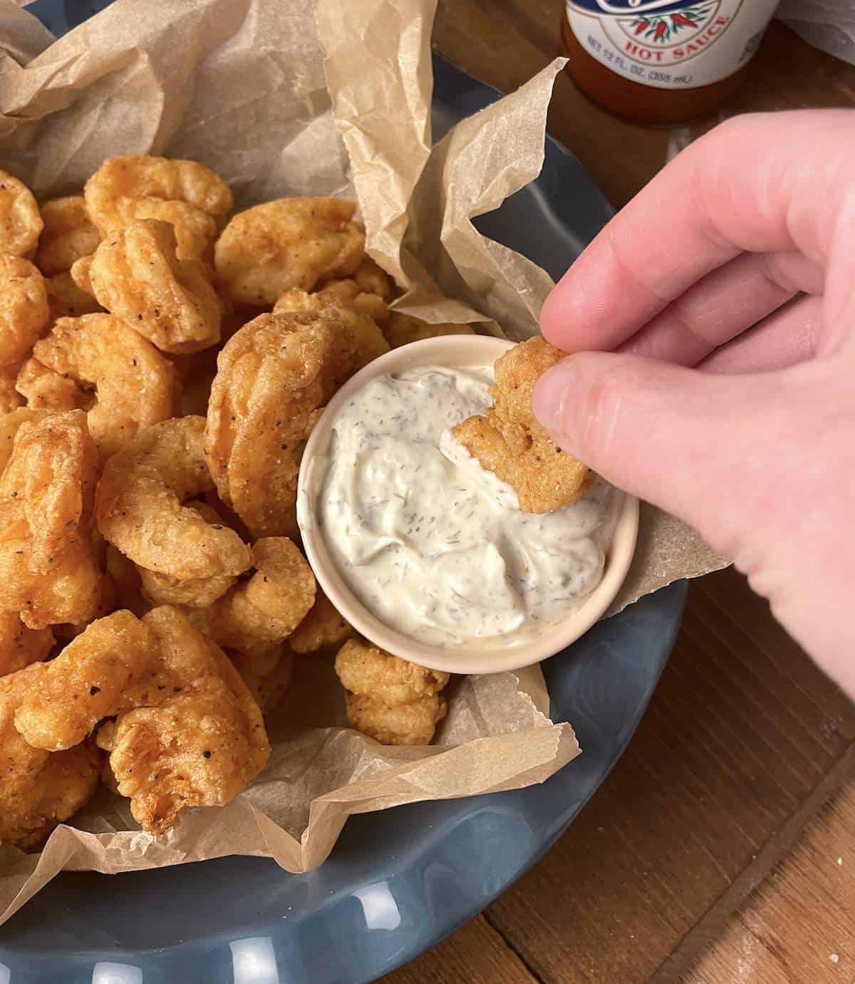 A bowl of fried shrimp with one shrimp being dipped in a small bowl of tartar sauce.