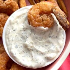 A small bowl of homemade tartar sauce with a fried shrimp in it.