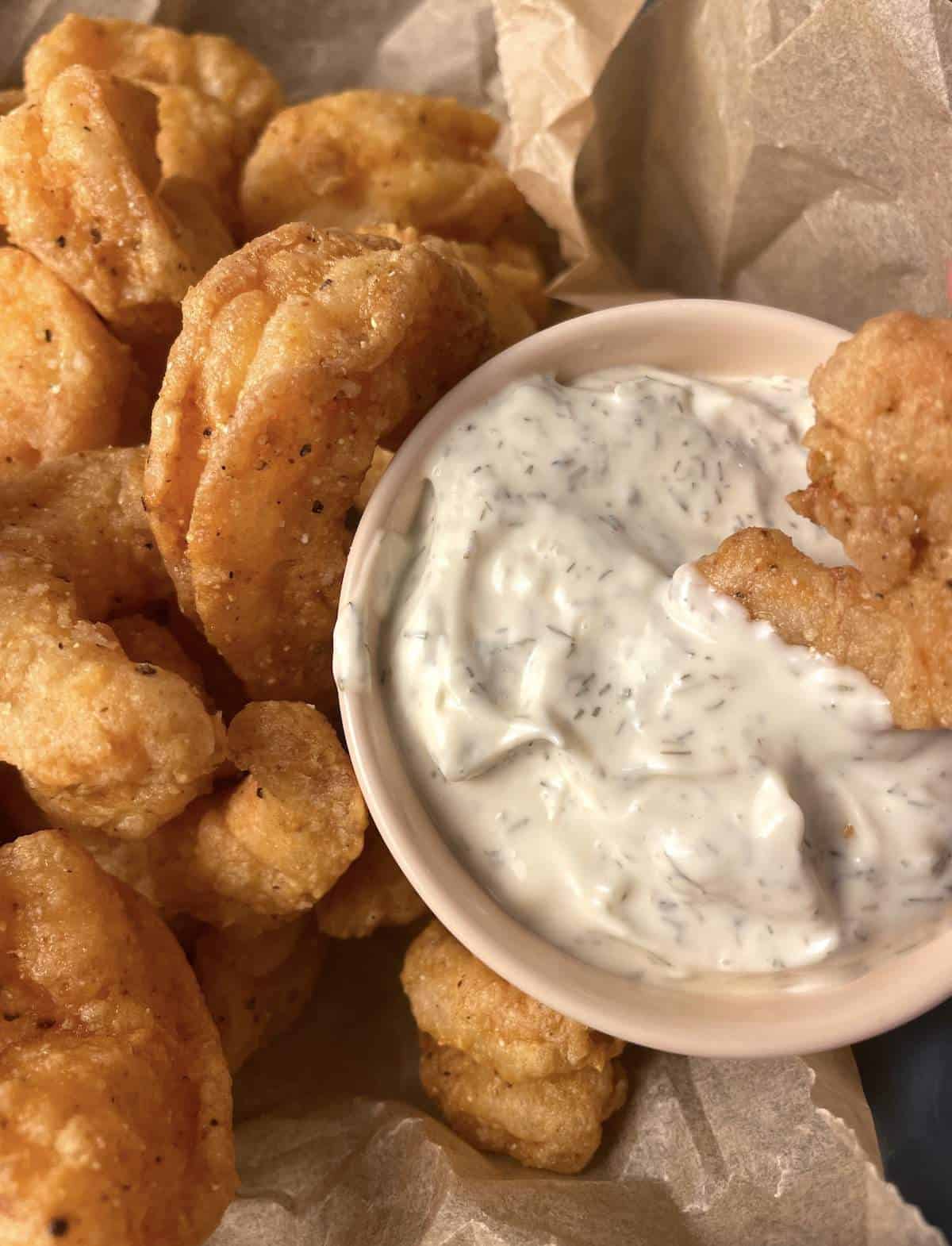 A bowl of popcorn shrimp with a small bowl of tartar sauce with a shrimp in it.