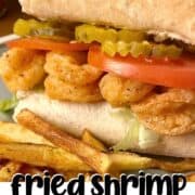 A pin image of a fully dressed fried shrimp po boy sandwich with extra pickles and crispy fries.