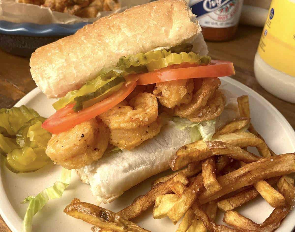 A fried shrimp po boy sandwich with extra pickles and crispy fries.