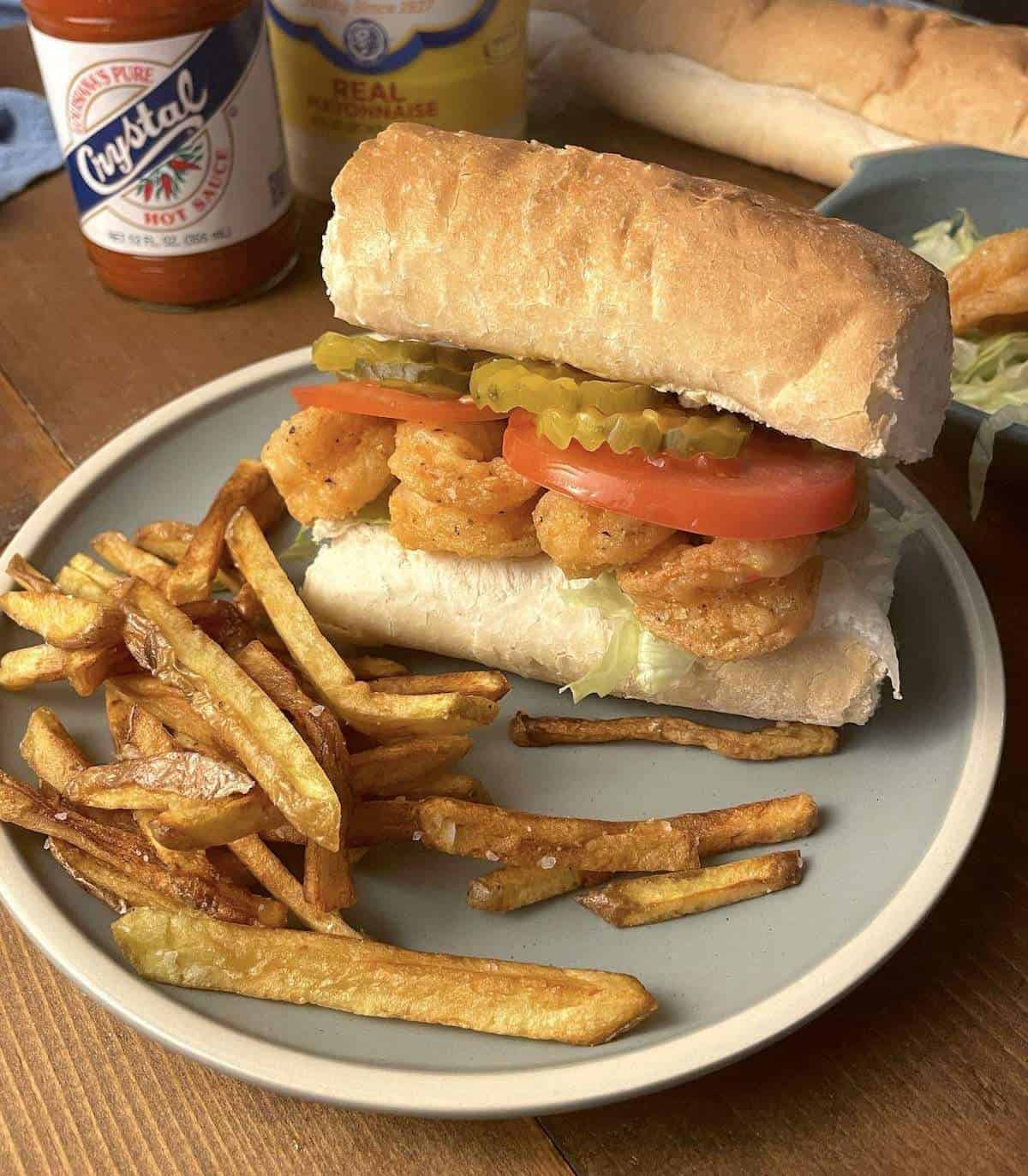 A fully dressed fried shrimp po boy on a blue plate with french fries.