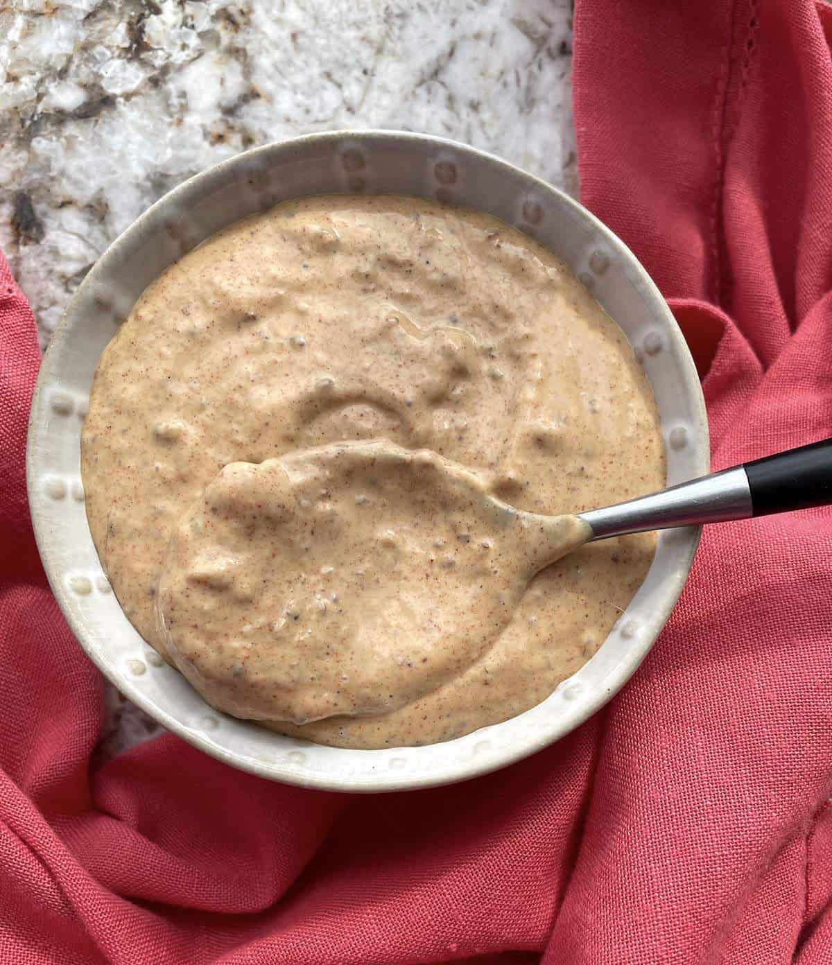 A bowl of remoulade sauce with a spoon in it.