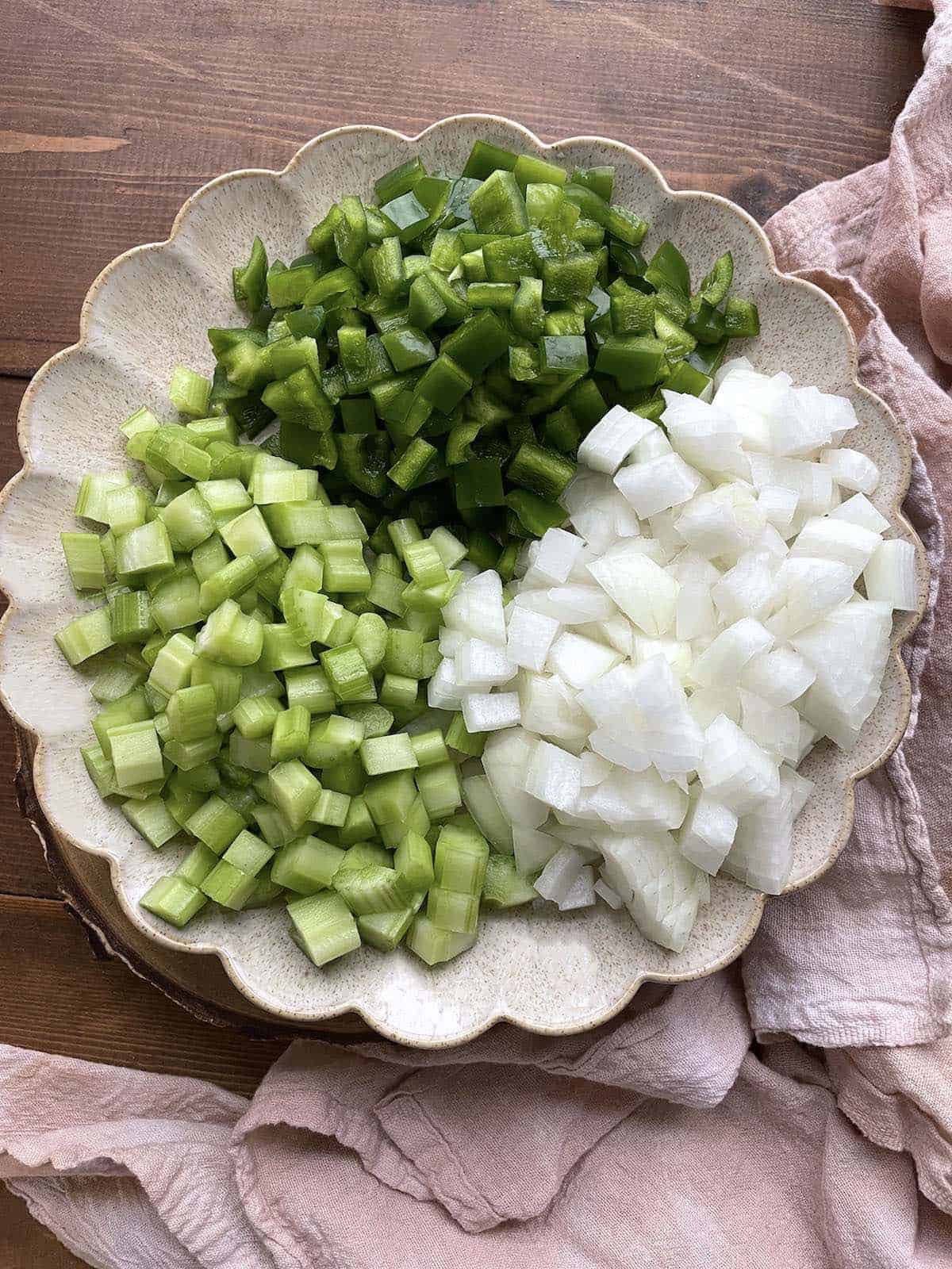 A plate of diced green bell peppers, onions, and celery to make the cajun holy trinity with a pink tea towel.