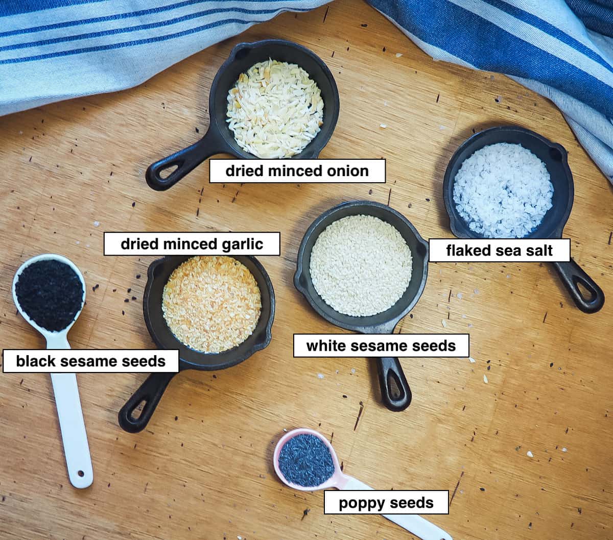 The ingredients in everything bagel seasoning laid out in small bowls and spoons and labeled.