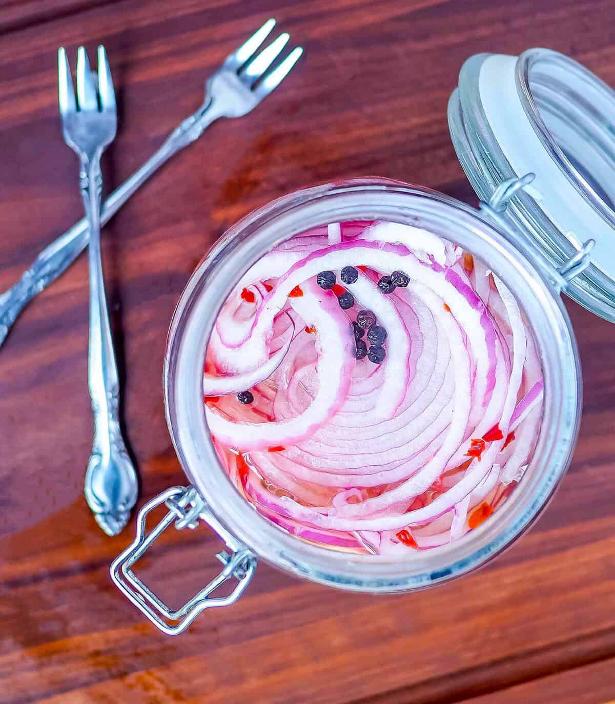 A jar of pickled red onions with peppercorns and two small forks.