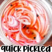 A jar of pickled red onions in brine with black peppercorns.