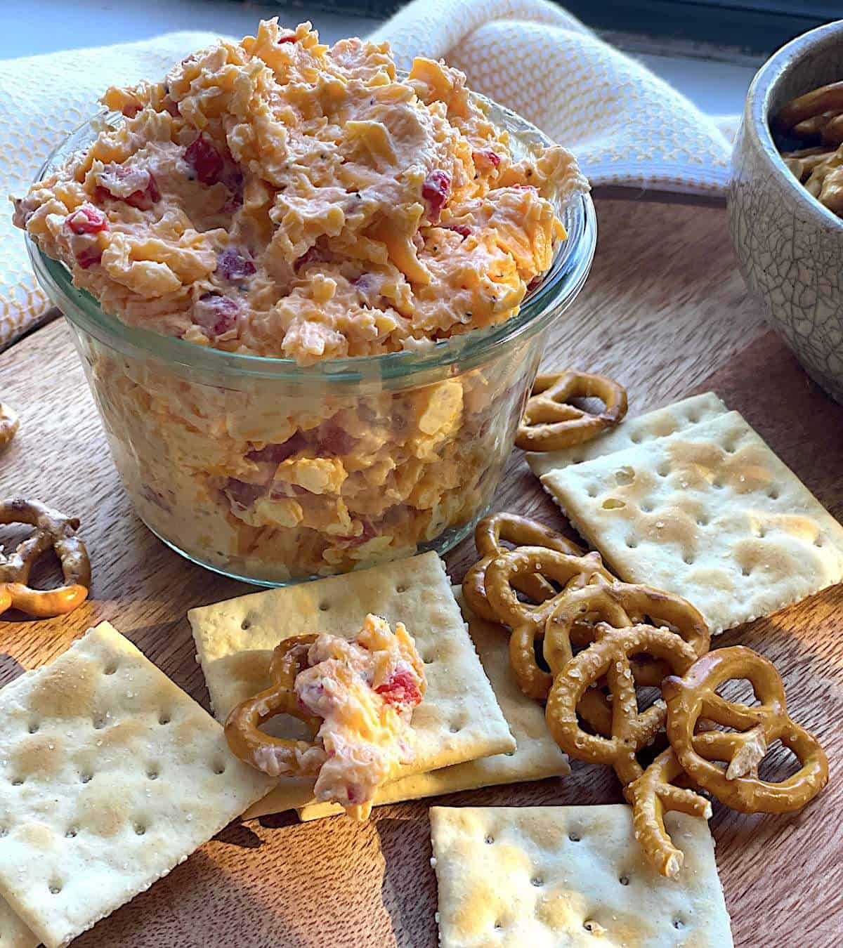 A glass bowl of homemade pimento cheese surrounded by pretzels and crackers.