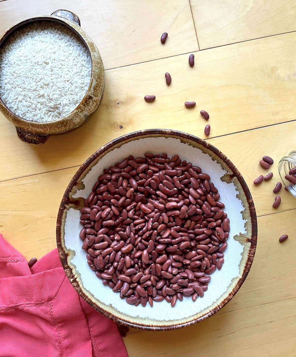 A bowl of dry red beans next to a small bowl of uncooked white rice.