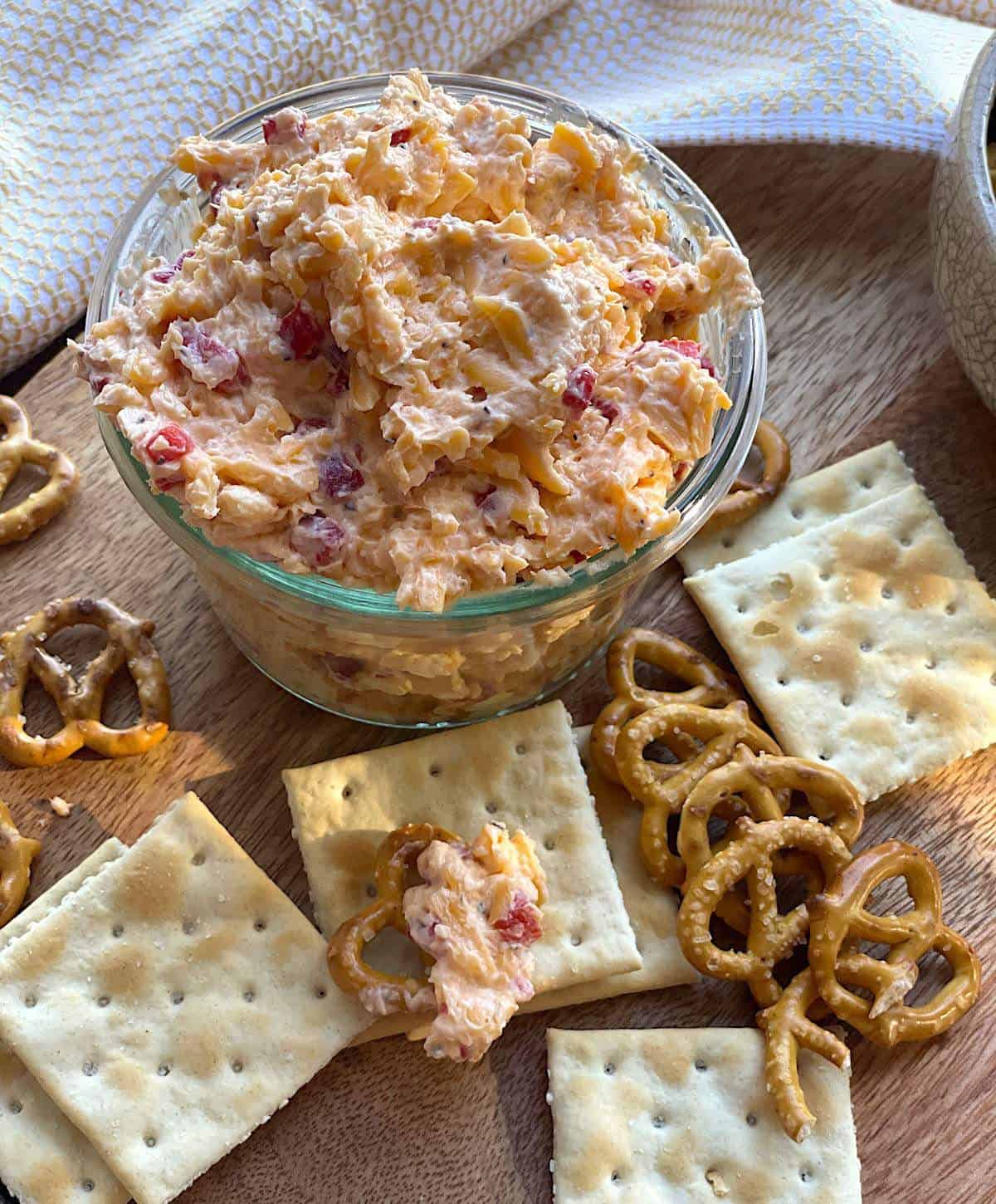 A glass bowl of homemade cheese spread surrounded by pretzels and crackers.