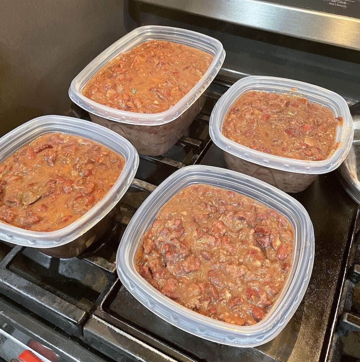 Cooked red beans and rice in plastic containers, cooling on a stovetop.
