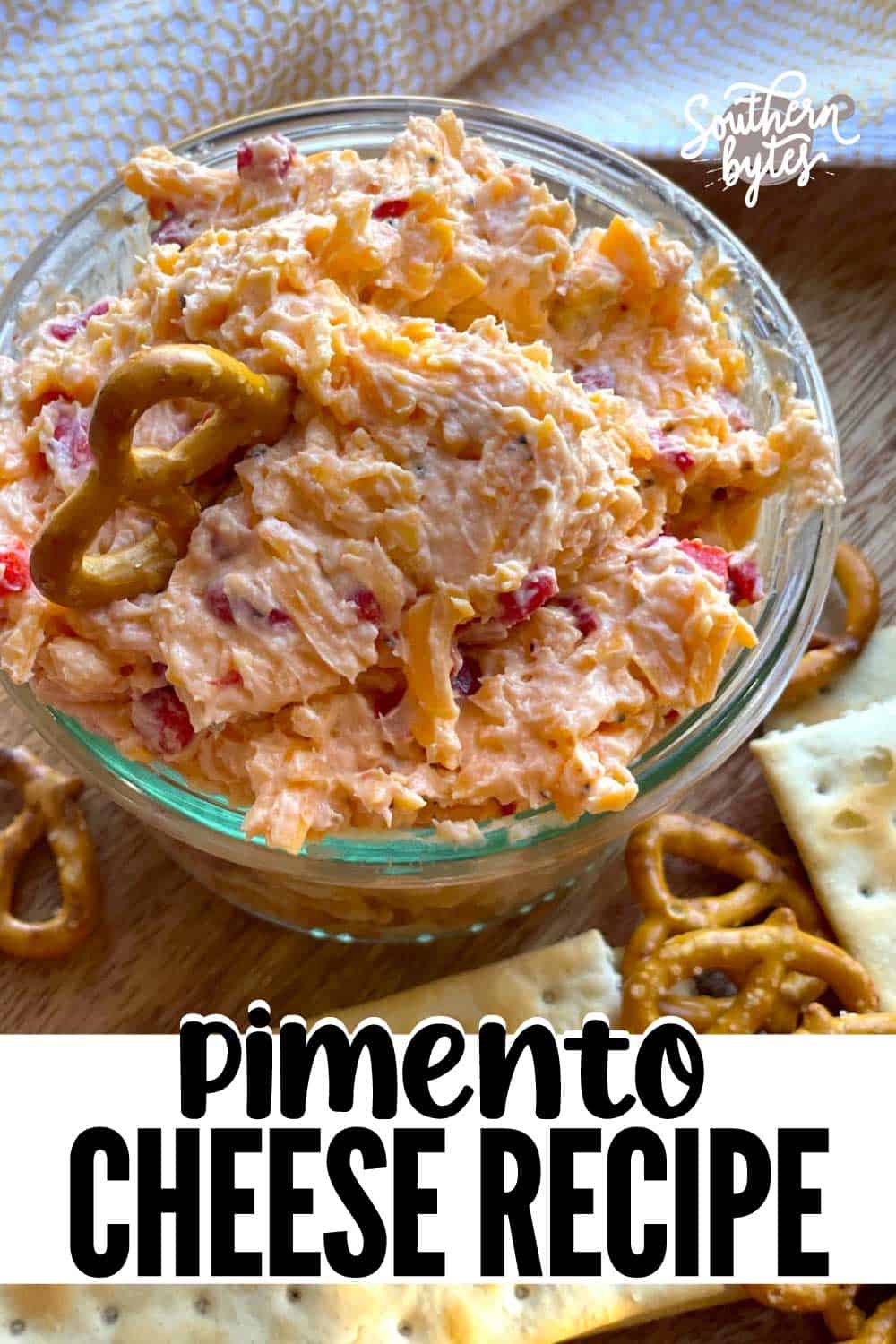 A pin image of a glass bowl of homemade pimento cheese surrounded by pretzels and crackers.