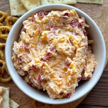 A white bowl of pimento cheese with pretzels and crackers around it.