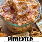 A pin image of a glass bowl of homemade pimento cheese surrounded by pretzels and crackers.